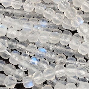 May include: A strand of white moonstone beads with a faceted, square shape. The beads have a translucent, milky white color with a slight iridescent sheen.