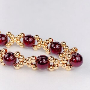May include: A close-up of a red gemstone bracelet with gold beads. The bracelet is made with alternating red gemstones and gold beads.