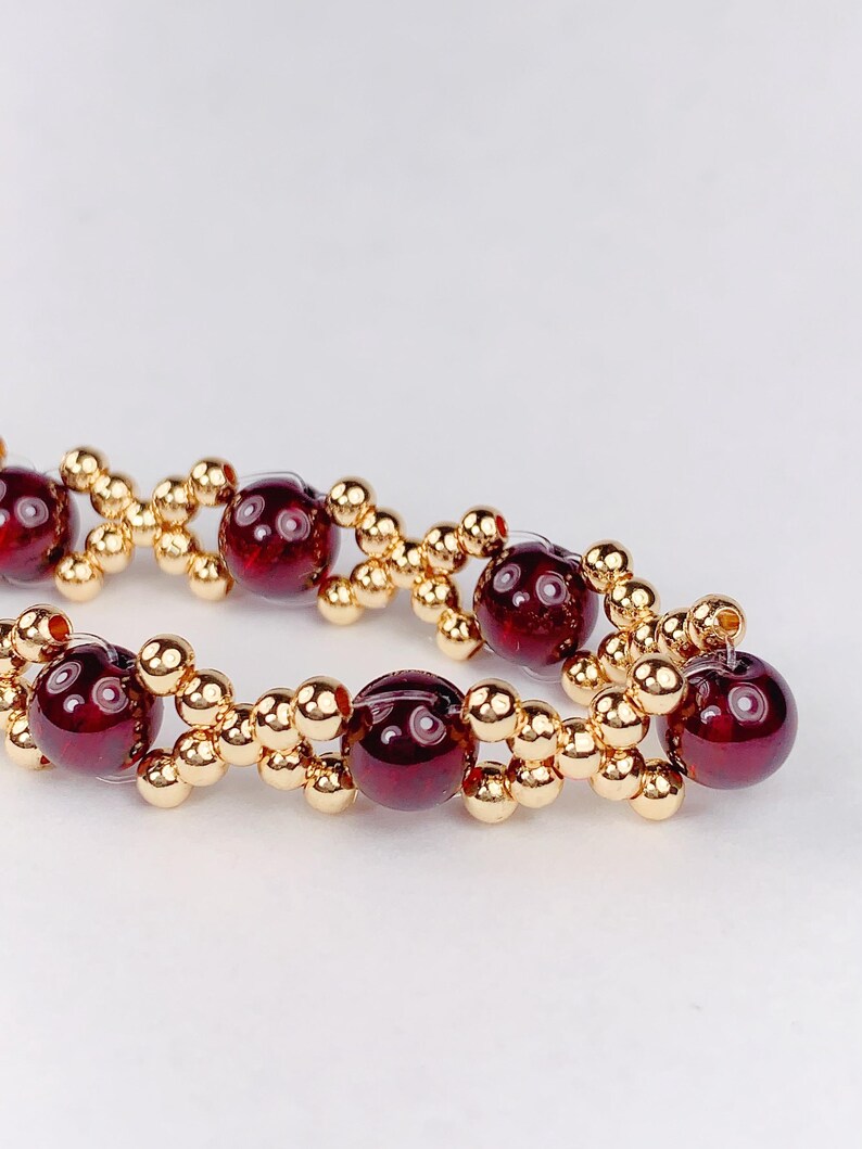 May include: A close-up of a red gemstone bracelet with gold beads. The bracelet is made with alternating red gemstones and gold beads.