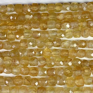 May include: Close-up of strands of faceted, golden-yellow gemstone beads. The beads are square-shaped with multiple facets, creating a sparkling effect. The color ranges from pale yellow to a deeper amber hue. The beads are strung together, ready for jewelry making.