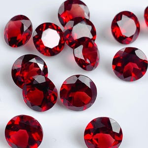 May include: A group of twelve round, red gemstones. The gemstones are faceted and have a shiny, polished finish.
