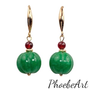 May include: A pair of gold dangle earrings with green jade and red glass beads. The jade beads are carved to resemble small pumpkins.