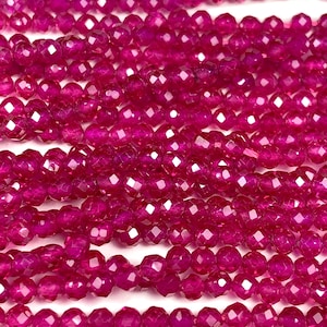 May include: Close-up of multiple strands of faceted, magenta-colored beads. The beads are small, round, and have a sparkling, polished appearance. The strands are arranged closely together, creating a dense, textured surface. The beads are likely used for jewelry making.