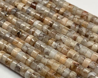 Può includere: Primo piano di fili di piccole perline sfaccettate nei toni del beige, marrone e grigio. Le perline sono di dimensioni e forma uniformi, creando una superficie strutturata. Le perline sono infilate, suggerendo che sono per la creazione di gioielli.