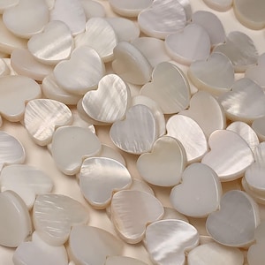 May include: A strand of white mother of pearl heart shaped beads. The beads are smooth and have a slight iridescent sheen.