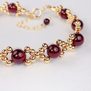 May include: A gold bracelet with red gemstone beads. The bracelet has a lobster clasp closure.