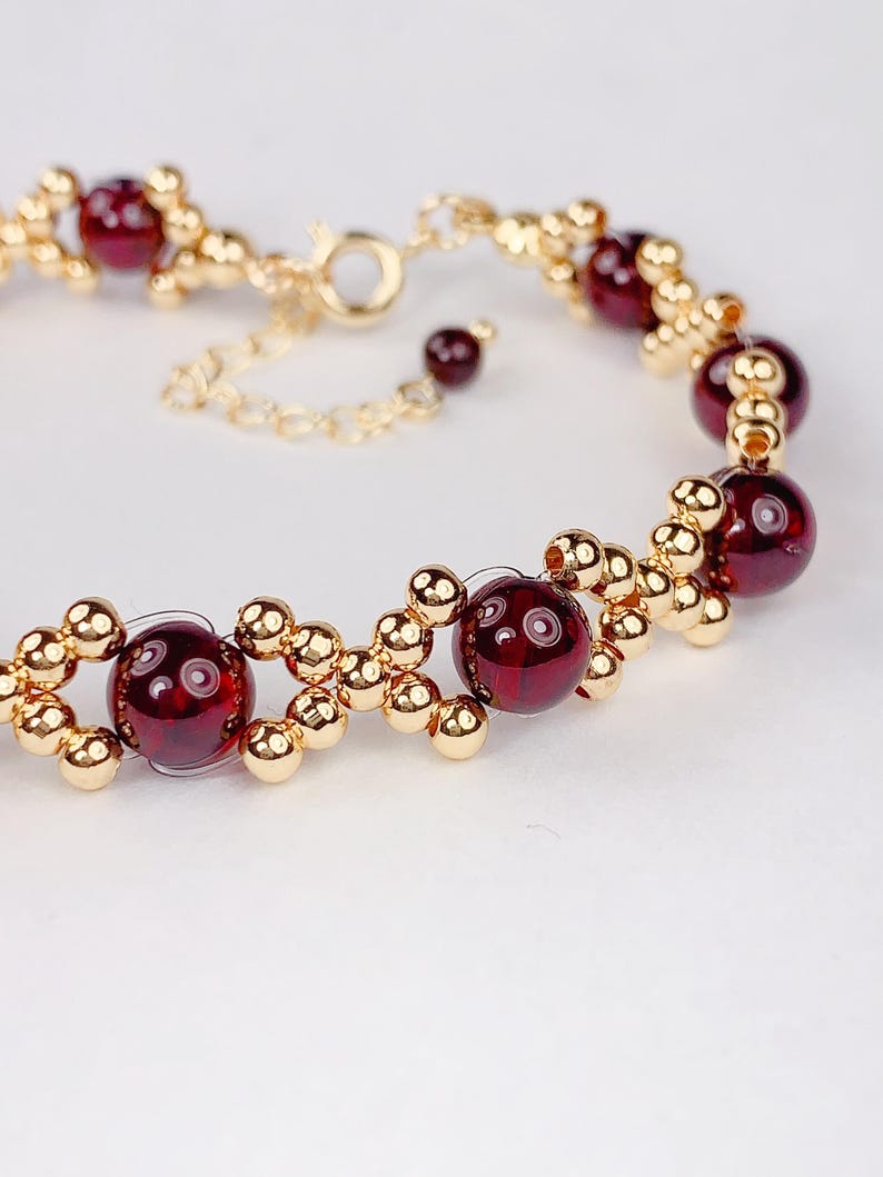 May include: A gold bracelet with red gemstone beads. The bracelet has a lobster clasp closure.