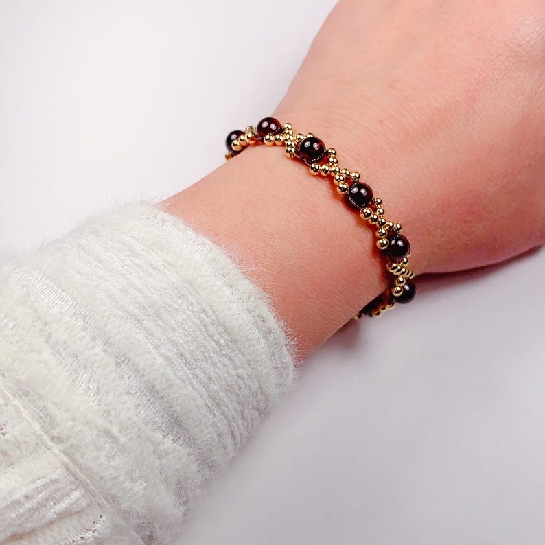 May include: A gold and dark red beaded bracelet with a criss-cross pattern.