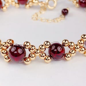 May include: A gold bracelet with red gemstone beads. The bracelet has a clasp closure.