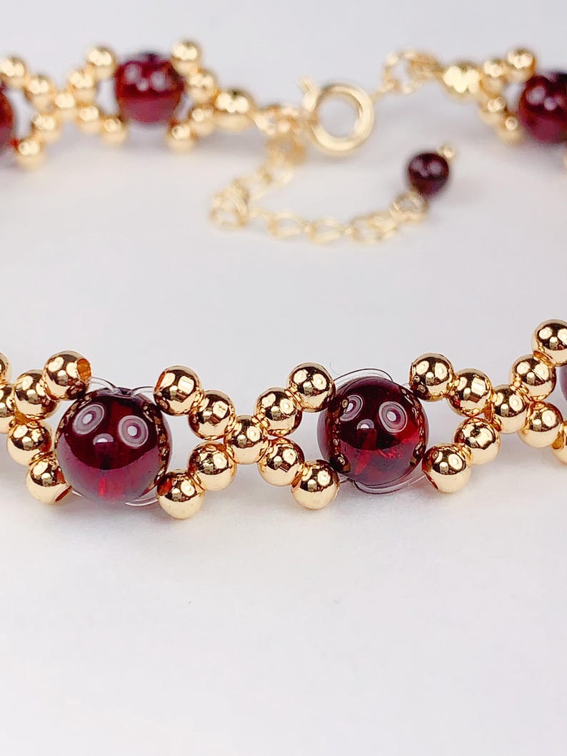 May include: A gold bracelet with red gemstone beads. The bracelet has a clasp closure.