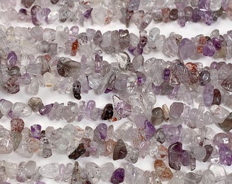 Op de afbeelding: Een streng kleine, onregelmatige, chip-vormige amethist kralen in tinten van paars, helder en wit. De kralen zijn getrommeld en hebben een natuurlijke, ruwe textuur.