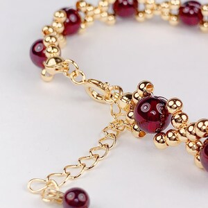 May include: A gold chain bracelet with red gemstone beads. The bracelet has a lobster clasp closure and an extender chain.