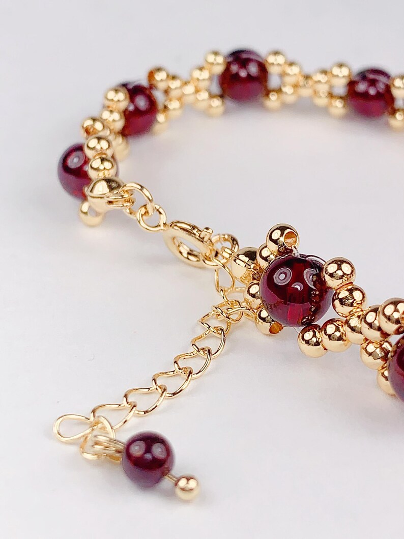 May include: A gold chain bracelet with red gemstone beads. The bracelet has a lobster clasp closure and an extender chain.