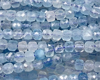 May include: A strand of light blue aquamarine gemstone beads. The beads are faceted and have a square shape. The beads are strung on a clear thread.