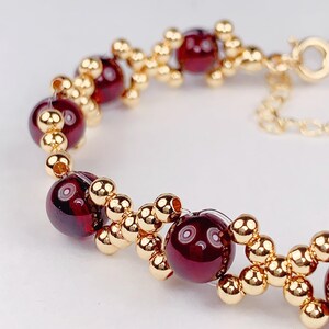 May include: A gold bracelet with red beads. The bracelet is made of small gold beads and larger red beads. The bracelet has a clasp.