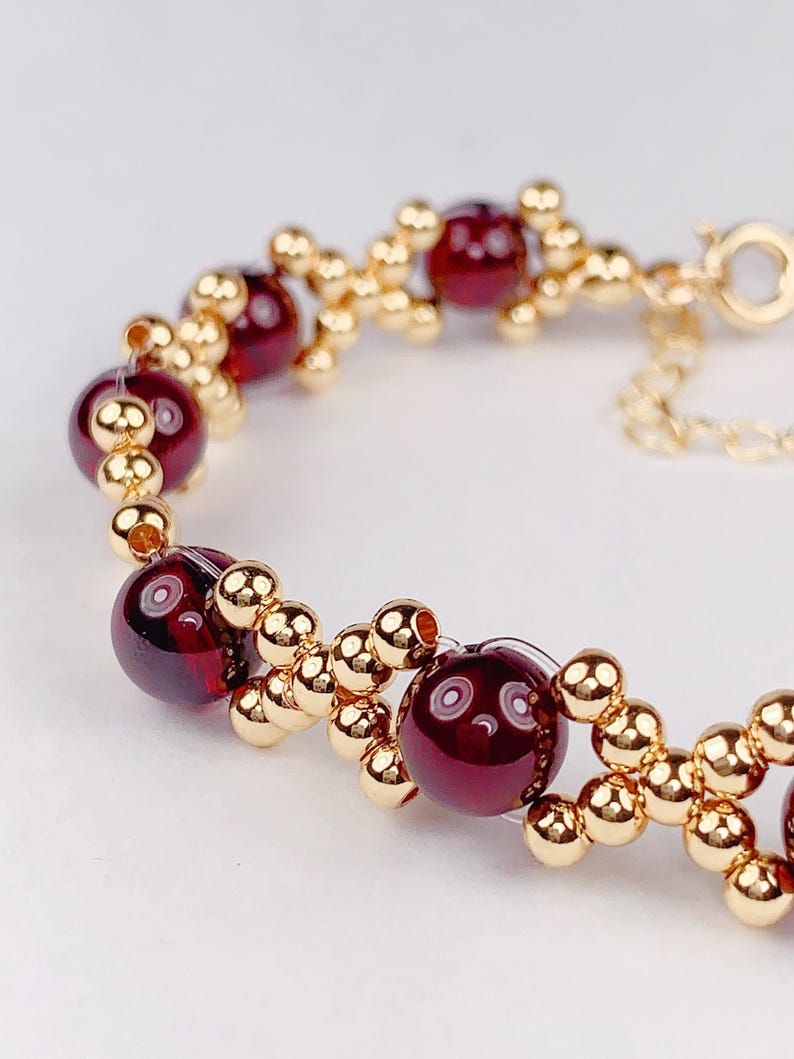 May include: A gold bracelet with red beads. The bracelet is made of small gold beads and larger red beads. The bracelet has a clasp.