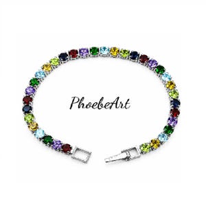 May include: A silver-toned tennis bracelet featuring a continuous row of round, multi-colored gemstones in shades of red, purple, green, yellow, and blue. The bracelet includes a secure metal clasp and the text PhoebeArt is centered.