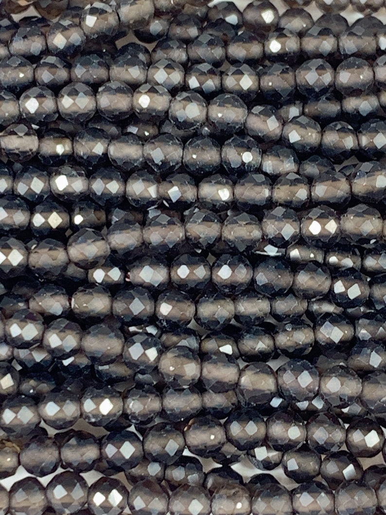 May include: A close-up of a strand of black faceted glass beads. The beads are round and have a smooth, polished finish.