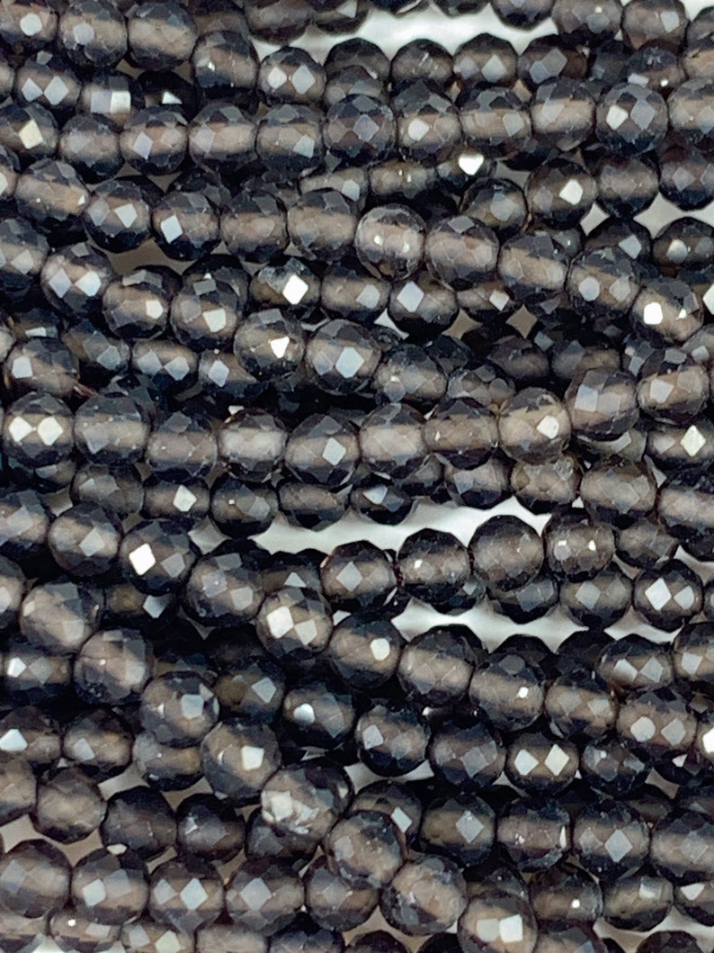 May include: A strand of black faceted glass beads. The beads are round and have a smooth, polished finish.