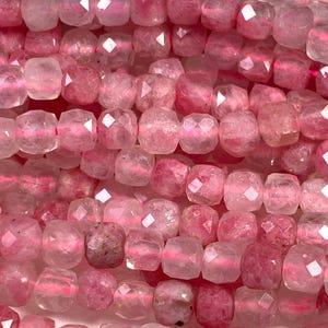 May include: Close-up of strands of pink gemstone beads. The beads are a mix of light and dark pink hues, with a faceted, square shape. The beads are strung together, creating a textured and colorful display. Ideal for jewelry making.