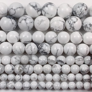 May include: A collection of white howlite beads with gray veining. The beads are round and smooth, and they are arranged in rows of different sizes. The beads are perfect for making jewelry or other crafts.