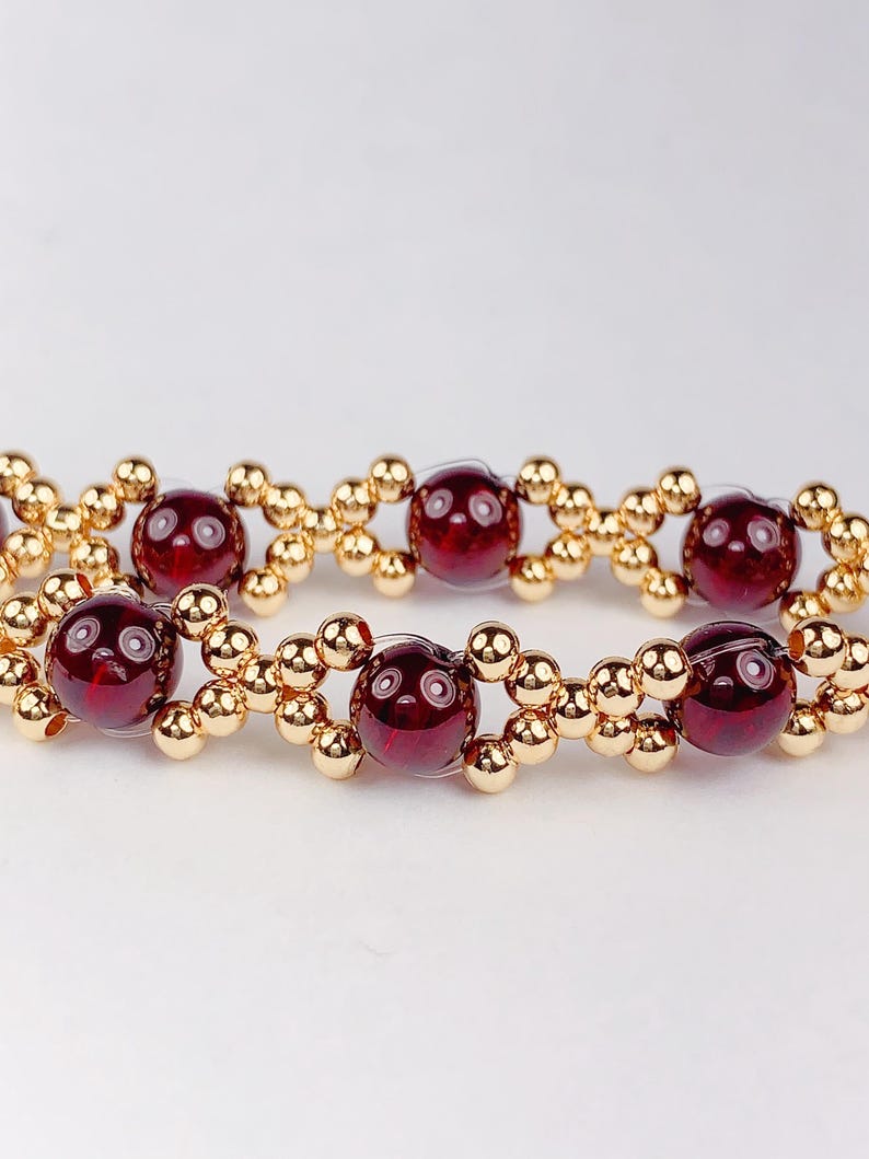 May include: A red gemstone bracelet with gold beads. The bracelet is made with round red gemstones and small gold beads.