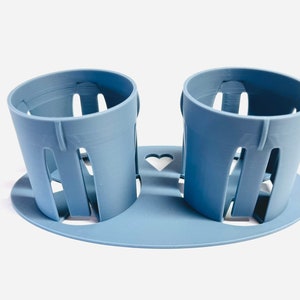 May include: A light blue plastic cup holder with two cups. The holder has a heart-shaped cutout in the center.