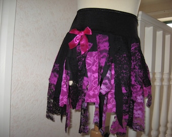 May include: A black and pink layered skirt with a pink bow. The skirt is made of lace and fabric strips.