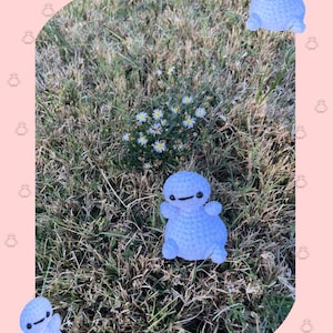 May include: A light blue crochet figure, resembling a cartoon character, is placed on a patch of grass with small white flowers. The image has the text "B-Max" and "Crochet Pattern" on a pink background.