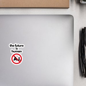 Peut inclure: Un ordinateur portable blanc avec un autocollant noir qui dit "the future is human" avec un cercle rouge et une ligne diagonale traversant le mot "A.I."