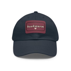 May include: A navy blue baseball cap with a red patch that says "bookworm" in a retro font with a pink heart.