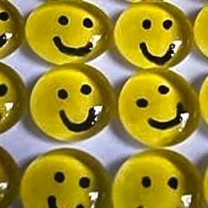 May include: A collection of yellow glass smiley face tiles with black painted features. The tiles are arranged in a circular pattern.