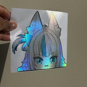 Pode incluir: Adesivo holográfico com um personagem em estilo anime com cabelo azul e prateado, olhos azuis e orelhas de raposa. O adesivo tem um acabamento brilhante e iridescente, criando um efeito arco-íris. O personagem tem uma boca pequena e sorridente.