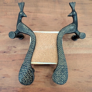 May include: Two black metal peacock door handles with gold accents. The handles are shaped like peacocks with their tails spread out. The handles are mounted on a wooden surface.