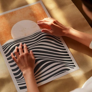 May include: A person is holding a black and white striped poster with a large white circle on a tan background. The poster has a wavy, optical illusion design.