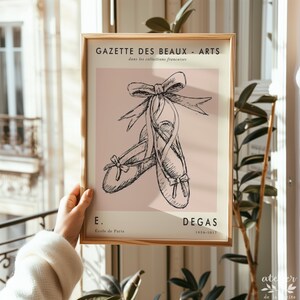 Pu&ograve; includere: Un poster in stile vintage con sfondo rosa che presenta un'illustrazione in bianco e nero di un paio di scarpette da balletto legate insieme con un fiocco. Il testo "GAZETTE DES BEAUX - ARTS" &egrave; in cima al poster, e il testo "E. Ecole de Paris" e "DEGAS 1834-1917" &egrave; in fondo.