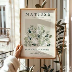 Pu&ograve; includere: Una stampa incorniciata di un'opera d'arte di Matisse intitolata "PAPIER D&Eacute;COUP&Eacute;S" che presenta un design astratto di foglie verdi, bianche e beige. La stampa &egrave; intitolata "GALERIE MAEGHT" e include il testo "Paris 1934" e "13 Rue de Teberan, Paris VIII".