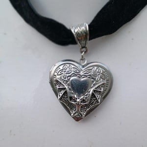 Könnte beinhalten: Eine silberne herzförmige Halskette mit einem Fledermaus-Design und floralen Akzenten. Die Halskette ist an einem schwarzen Samt-Choker.