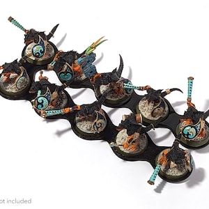 May include: A black plastic storage tray with eight circular compartments, each holding a miniature painted figure. The figures are black, blue, and gold, and are mounted on round bases.