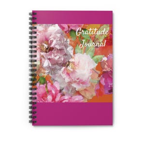 May include: A pink and orange gratitude journal with a floral design on the cover. The journal has a spiral binding and the words "Gratitude Journal" are printed in white on the cover.