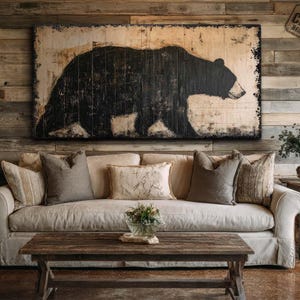 May include: A rectangular canvas wall art piece featuring a large, black silhouette of a bear against a distressed, light-colored background. The artwork is mounted on a wall constructed of horizontal wooden planks, positioned above a beige sofa.