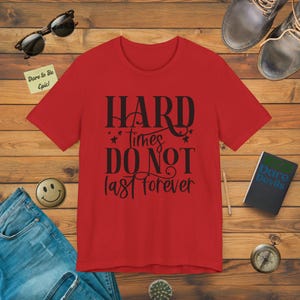 Puede incluir: Camiseta roja con texto negro que dice "Hard times do not last forever".