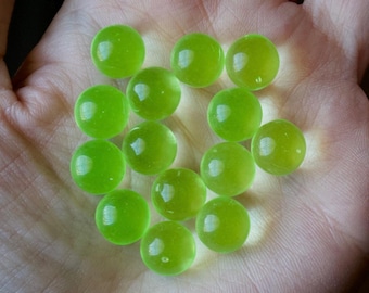 May include: A collection of 12 green glass marbles, some with a slight yellow tint, are scattered on a hand.