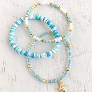 May include: Three bracelets with blue and white beads. The smallest bracelet has a gold starfish charm.
