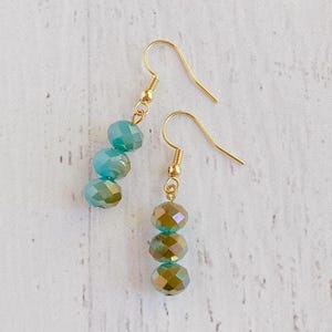 May include: A pair of gold dangle earrings with three iridescent green glass beads on each earring.