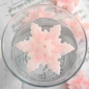 May include: A pink snowflake-shaped floating candle in a glass bowl filled with water.