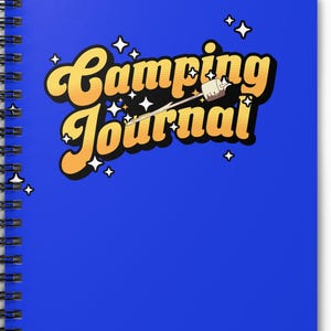 Può includere: Un quaderno blu a spirale con la scritta "Camping Journal" in un font retrò dorato con contorno bianco. Il design include una grafica di marshmallow su uno stecchino e piccole stelle bianche. Per appunti di campeggio.