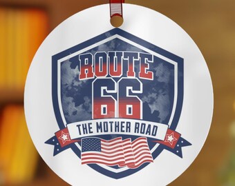 Op de afbeelding: Ronde witte kerstbal met een blauw en rood schildontwerp. Het schild heeft de tekst "ROUTE 66 THE MOTHER ROAD" en een gestileerde Amerikaanse vlag.