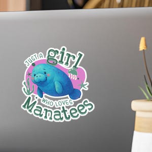 May include: A sticker featuring a blue manatee illustration with the text "Just a girl who loves Manatees." The design includes pink and green accents, with a cartoon-style aesthetic. The sticker is on a laptop.