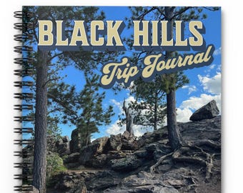May include: Spiral-bound notebook with a cover featuring the text "BLACK HILLS Trip Journal" in a vintage style. The cover image shows a scenic view of the Black Hills with trees, rocks, and a blue sky with clouds.